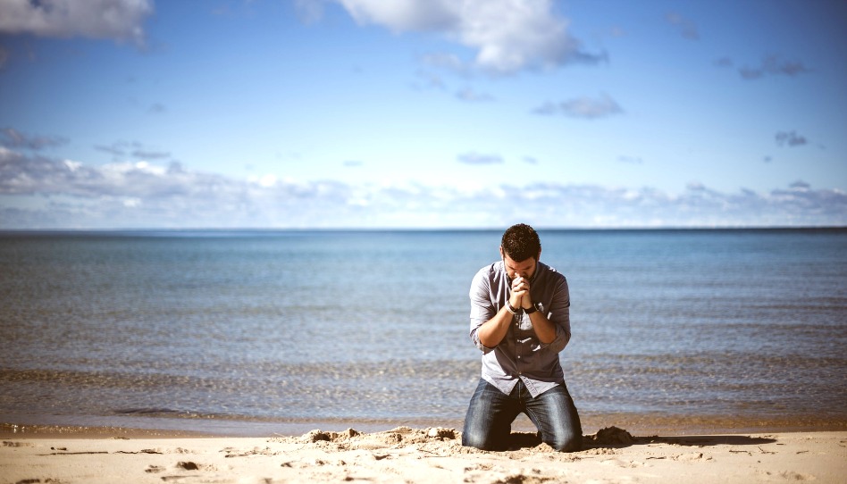 Mann kniet betend am Strand